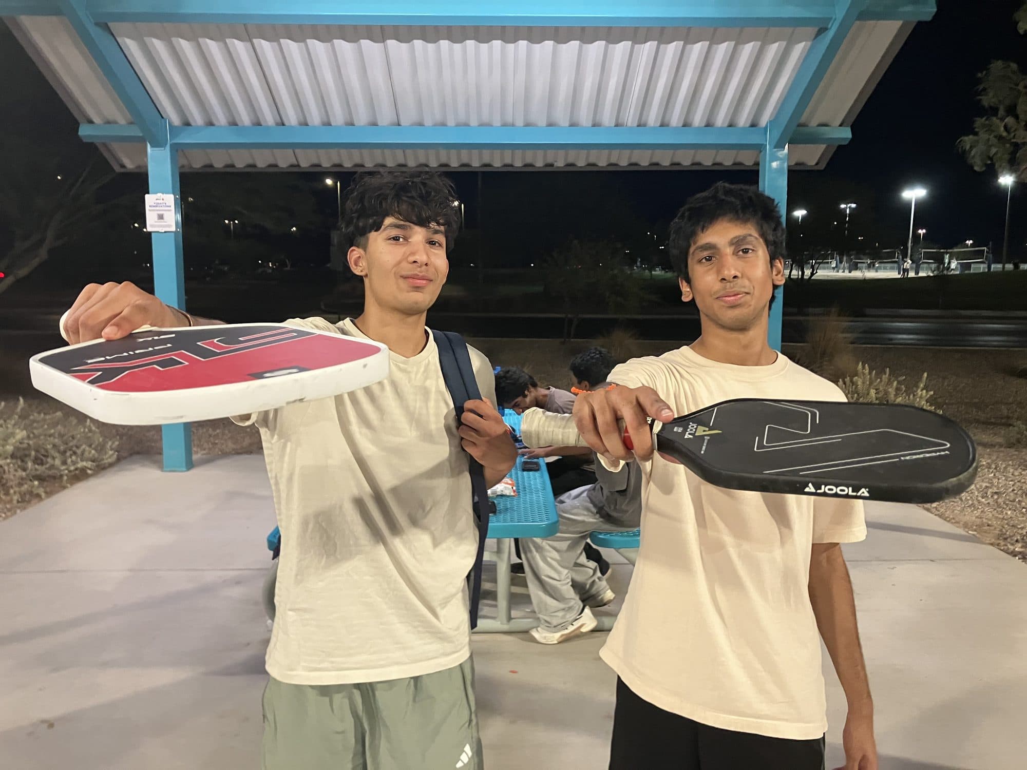 Two ALS Forward players holding up their paddles at the courtside ramada after a match