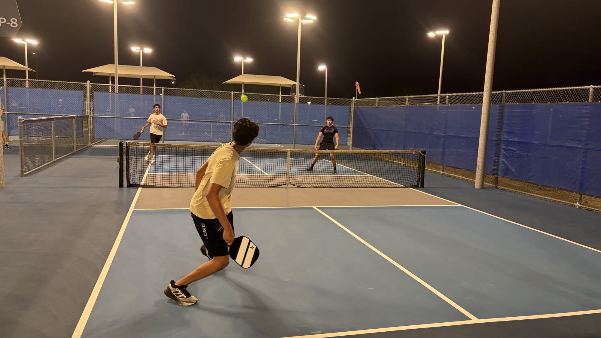 A player mid-swing at the back of the court with the ball in the air and two opponents at the net